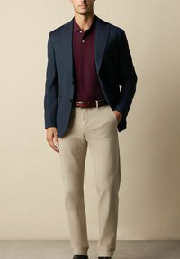 Námořnický blazer přes bordó polo, v kombinaci s béžovými kalhotami a hnědým opaskem. Hladká tkanina s pravidelným střihem a klasickými detaily.