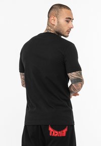 Camiseta de algodón negra con mangas cortas y cuello redondo. Presenta una textura suave. La vista trasera no muestra logotipos ni patrones visibles.