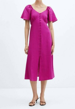 Femme portant une robe midi magenta à manches bouffantes et boutons sur le devant, associée à des sandales marron à talons avec brides, sur fond blanc.