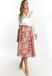Blusa in satin bianca abbinata a una gonna midi con design a stampa leopardata rossa. La gonna scivola con pieghe visibili e una vita elastica.