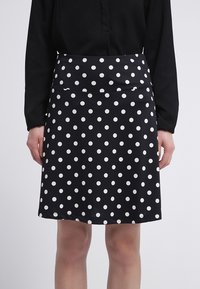 Falda negra con lunares blancos, tela suave, forma clásica en A, de longitud media con una cintura lisa y sin cierres visibles.