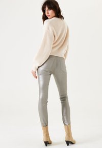 Lichtbeige gebreide trui met een dropped shoulder en een gestructureerde stof, gecombineerd met strakke metallic zilveren broeken en taupe enkellaarzen.