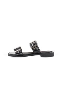 Sandalias planas negras que cuentan con dos correas ajustables con hebillas metálicas y acentos de ojales. Textura lisa y diseño minimalista.