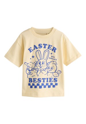 Gelbes Kurzarmshirt mit blauem Cartoon von einem Hasen, Lamm und Küken und dem Text "Easter Big Smiles Besties" auf der Vorderseite.