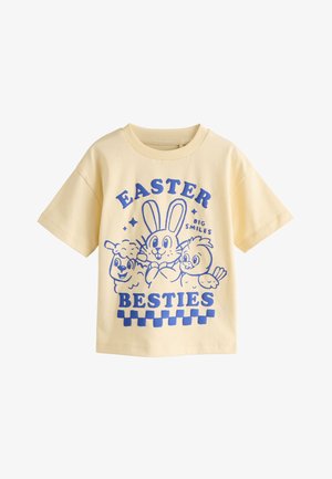 Geel T-shirt met korte mouwen met een blauwe cartoon van een konijn, lammetje en kuiken, en tekst "Easter Big Smiles Besties" op de voorkant.