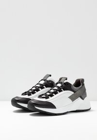Sneakers sportive con tomaia in pelle bianca e nera, sottili accenti grigi, lacci testurizzati e una spessa suola in gomma bianca.