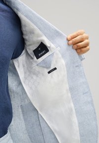 Helles blaues, gemustertes Innenfutter der Jacke mit strukturiertem Finish. Sichtbare Etiketten: "JOOP!" und "SLIM FIT." Das äußere Material erscheint glatt.
