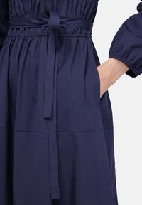 Abito blu navy con vita elastica, cintura abbinata e maniche arricciate. Texture morbida, presenta tasche laterali e design a pannelli.