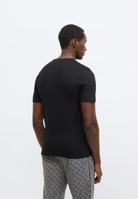 Musta lyhythihainen t-paita, valmistettu puuvillasta, yksinkertaisella pyöreällä pääntiellä ja istuvalla mallilla. Yhdistetty kuvioituihin harmaisiin housuihin.