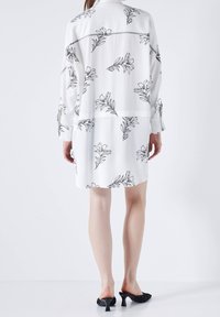 Abito bianco con maniche lunghe e un fit rilassato, decorato con motivi floreali neri, abbinato a mule nere con tacco.