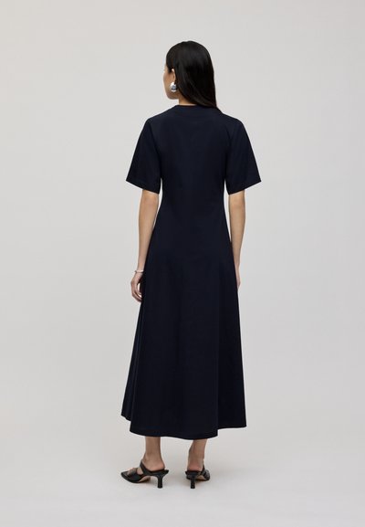 Granatowa bawełniana sukienka maxi z krótkimi rękawami, okrągłym dekoltem i zwiewnym krojem A-linii. Charakteryzuje się długością do połowy łydki oraz minimalnymi detalami.