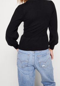 Haut noir moulant en maille avec manches bouffantes, texture côtelée et taille marquée, associé à un jean taille haute bleu clair avec poches arrière.