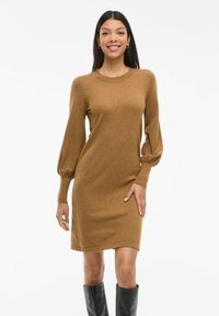 Brown knit dress with a crew neck, long puff sleeves, and a fitted silhouette. Paired with knee-high black boots. Smooth texture.