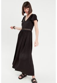 Abito maxi nero con maniche a volant corte, scollo a V e un nastro decorativo in pizzo all'altezza della vita. Tessuto morbido e gonna fluida.