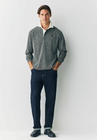 Langærmet grå sweater med et tekstureret mønster, hvid krave og navyblå jeans, parret med sorte loafers. Model står oprejst.