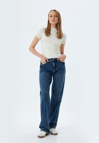Top bianco a maniche corte con righe e scollatura a onda abbinato a jeans a gamba larga blu sbiaditi e sneakers bianche con suola beige.