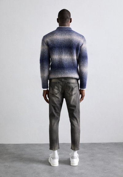 Strikkegenseren har et gradient av blå og hvite striper, brukt sammen med grå jeans og hvite sneakers. Designet inkluderer høy krage og ribbestrikkede ermer.