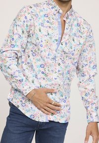 Chemise à boutons florale avec un fond pastel clair parsemé de petites fleurs multicolores, à manches longues et avec une patte de boutonnage contrastante.