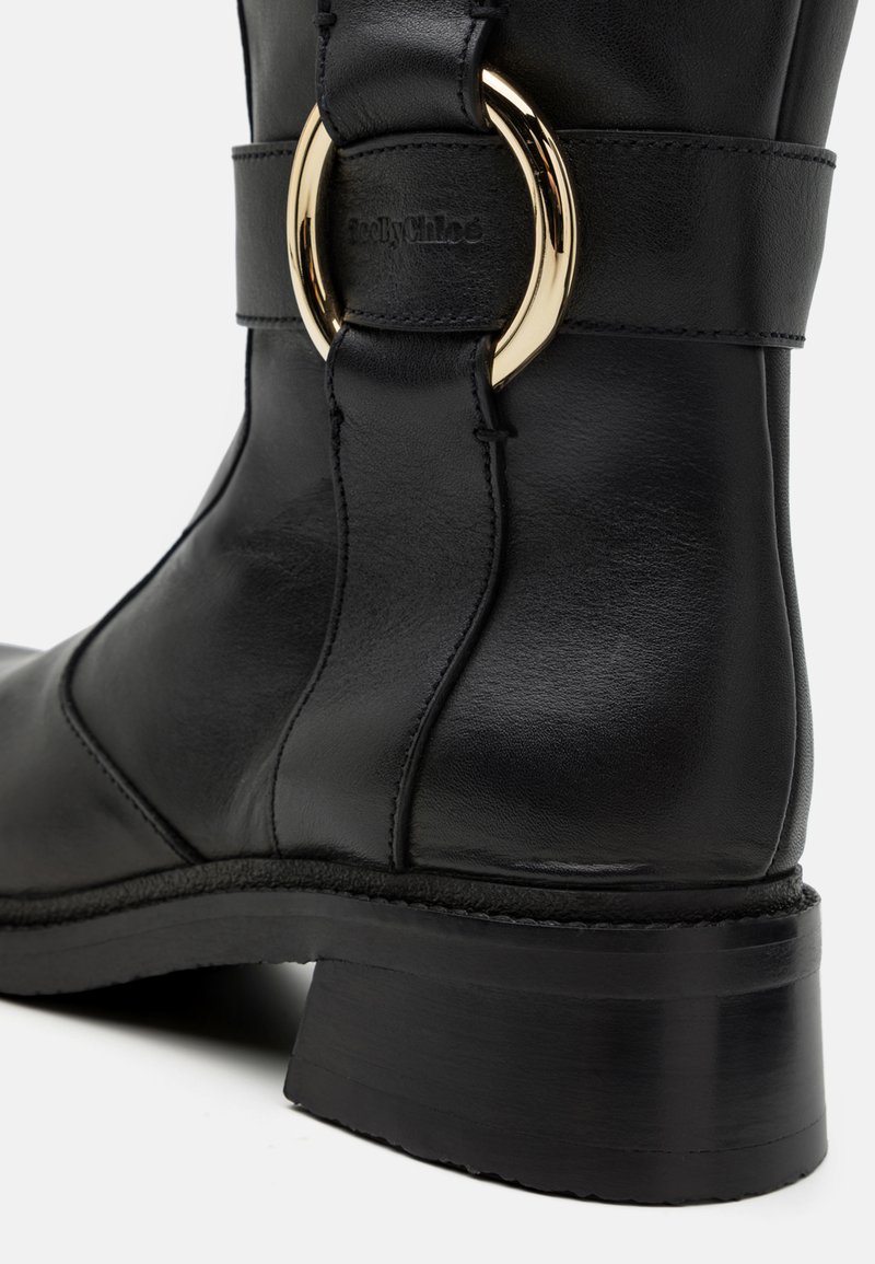 Schwarze Lederstiefel mit runder Zehenform, sanftem Glanz und einem goldenen, runden Schnallenakzent am Riemen. Niedriger schwarzer Absatz.