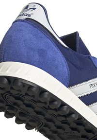 Modré tenisky Adidas s svrchní částí z semiše a textilu, bílymi pruhy a texturovanou černou gumovou podrážkou s výraznými výstupky.