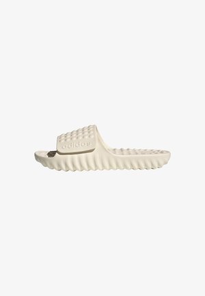 Sandale slide Adidas en blanc cassé avec une tige texturée, un design de semelle ondulée et un logo de marque en relief ; fabriquée à partir d'un matériau doux et flexible.
