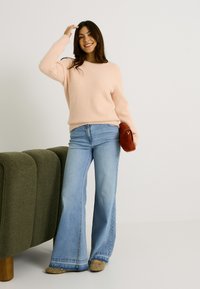 Pull en peluche rose clair, jean bleu à jambes larges, et sac marron. Pull texturé, jean décontracté avec un ourlet effiloché et chaussures à clous.