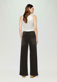 Black wide-leg jeans with back pockets, paired with a metallic silver sleeveless top, highlighting a smooth texture and modern silhouette.