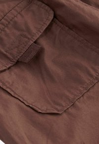 Tissu brun avec une texture lisse, comportant une poche à rabat avec des détails cousus. Le matériau semble léger et légèrement réfléchissant.