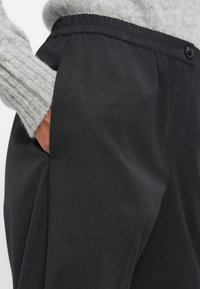 Zwarte broek met een elastische tailleband en zijzak. Gemaakt van een gladde stof met een subtiele glans, voorzien van nette plooien.