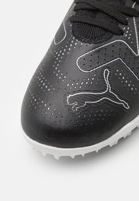 Scarpa da calcio sintetica nera con micro-perforazioni, cuciture bianche e suola in gomma bianca con piccoli tacchetti. Logo Puma in evidenza.