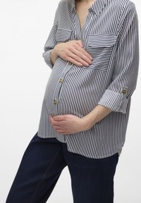 Stripet skjorte i marineblå og hvid med to brystlommer, op-rullede ærmer og en afslappet pasform, parret med mørke denimbukser.