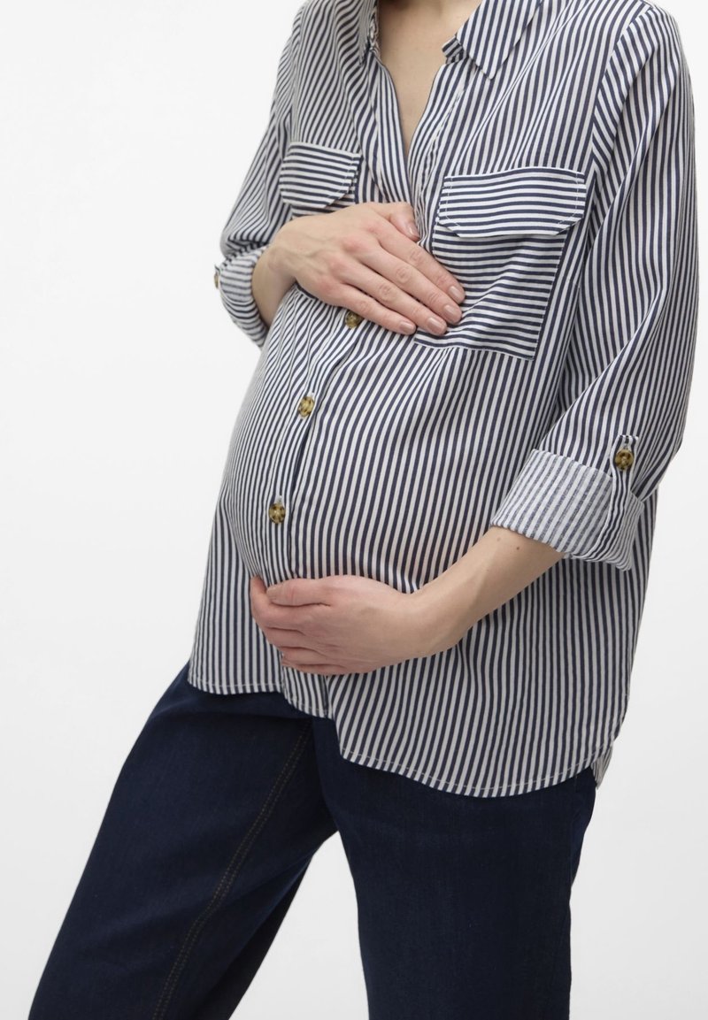 Stripet skjorte i marineblå og hvid med to brystlommer, op-rullede ærmer og en afslappet pasform, parret med mørke denimbukser.
