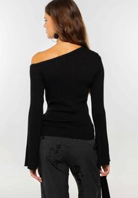 Top de punto acanalado negro, con escote off-shoulder y mangas largas de campana, que presenta una silueta ajustada. La textura tiene ligeros acentos de brillo.