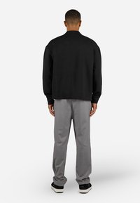 Black textured sweater with a relaxed fit, paired with gray trousers and black sneakers, viewed from behind against a white background.