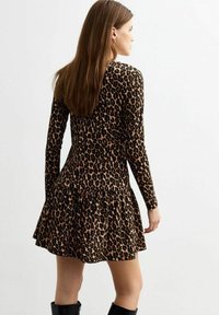 Vestido de leopardo de manga larga con falda acampanada, que presenta un cuerpo ajustado y una textura de tela suave. Los colores incluyen negro, marrón y crema.