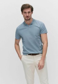 Ljust blå polo med krage, korta ärmar och slim fit, tillsammans med vita byxor och ett brunt bälte. Enkelt design, inga mönster.