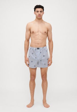 Pantaloni za boks s prugastim vzorcem iz bombaža in elastičnim pasom, okrašeni z majhnimi risanimi motivi v modri in rdeči barvi na beli podlagi.