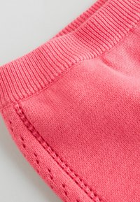 Pinky színű pamutszövet, bordás derékpánttal és díszvarrott szélekkel. Sima textúra, egyenletes szín és folyamatos varrás jellemzi.