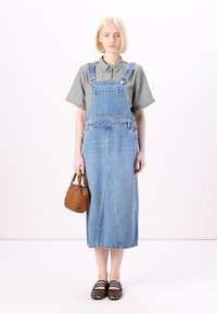 Lys blå denim overallkjole med en rett silhuett, med en frontlomme, kombinert med en grå kortermet skjorte og en brun veske.