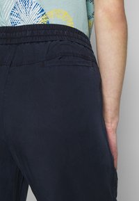 Marineblauwe broek met elastische tailleband, voorzien van een achterzak, een gladde textuur en een casual ontwerp. De stof lijkt licht en ademend te zijn.