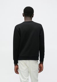 Μαύρο φούτερ με στρογγυλή λαιμόκοψη και ρ ιμπ μανσέτες. Το ύφασμα φαίνεται υφασμάτινο και παχύ. Φορεμένο με τζιν ανοιχτού χρώματος.