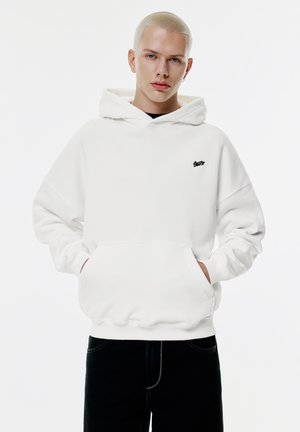 Weißer Pullover-Hoodie mit einer vorderen Kängurutasche, lässiger Passform und schwarzem Logodesign auf der Brust. Weiche Textur und mittlere Dicke.