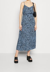 Maxi šaty s potiskem zebry v modré a černé barvě, s tenkými ramínky, volným střihem a délku po calf, doplněné černými chunky platformovými botami.