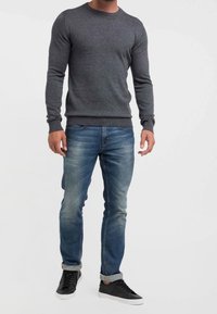 Grauer Strickpullover mit Rundhalsausschnitt, kombiniert mit blauen Denim-Jeans mit leichtem Used-Effekt. Schwarze Sneaker mit weißen Sohlen vervollständigen das Outfit.