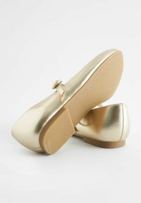 Ballerine metallizzate dorate con punta arrotondata, cinturino alla caviglia e tacco basso a blocco. La suola presenta un motivo di grip testurizzato.
