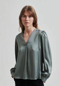 Halenka s long-sleeve v tlumené zelené saténové barvě, V-výstřihem a nařasenými rukávy, s volným střihem a jemnými sklady vpředu.