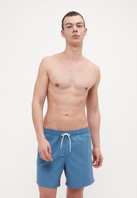 Shorts de bain bleus avec une taille élastique et un cordon de serrage blanc. Le tissu semble léger et doux avec une coupe ajustée.