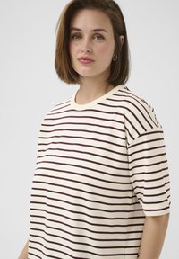 Striped t-shirt in cream with dark brown horizontal stripes. Features a round neckline and short sleeves. Soft texture, loose fit.