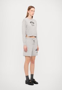 Sweatshirt cinzento cortado com um logótipo preto, combinado com calções cinzentos com cordão na cintura e bolsos laterais. Mocassins pretos e meias cinzentas.