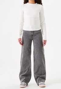 Top blanco de manga larga con canalé acompañado de unos vaqueros oscuros de corte holgado. Conjunto completado con zapatillas grises con detalles en blanco.
